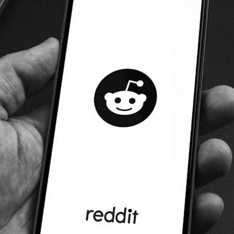 Man holding a smartphone with Reddit social media app on the screen on black background table. Office environment.