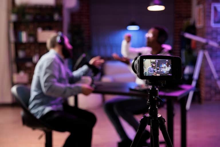 monetization guide - Focus shot on professional camera used to record podcast show with presenter and guest discussing in blurry background. Equipment in home studio used for live streaming broadcast