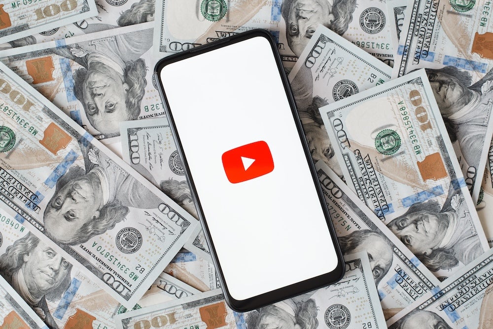 YouTube demonetization - a phone showing the YouTube logo sitting on a stack of money 