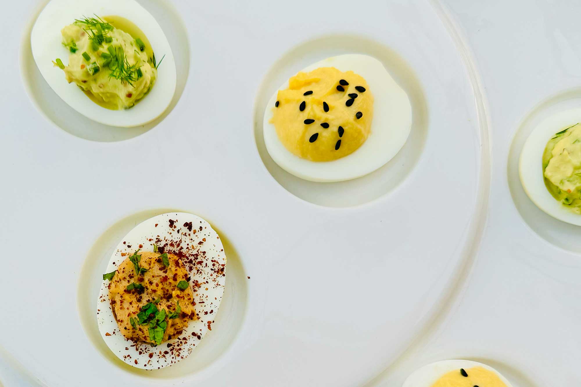 Three deviled eggs on a counter with various toppings on a grey counter