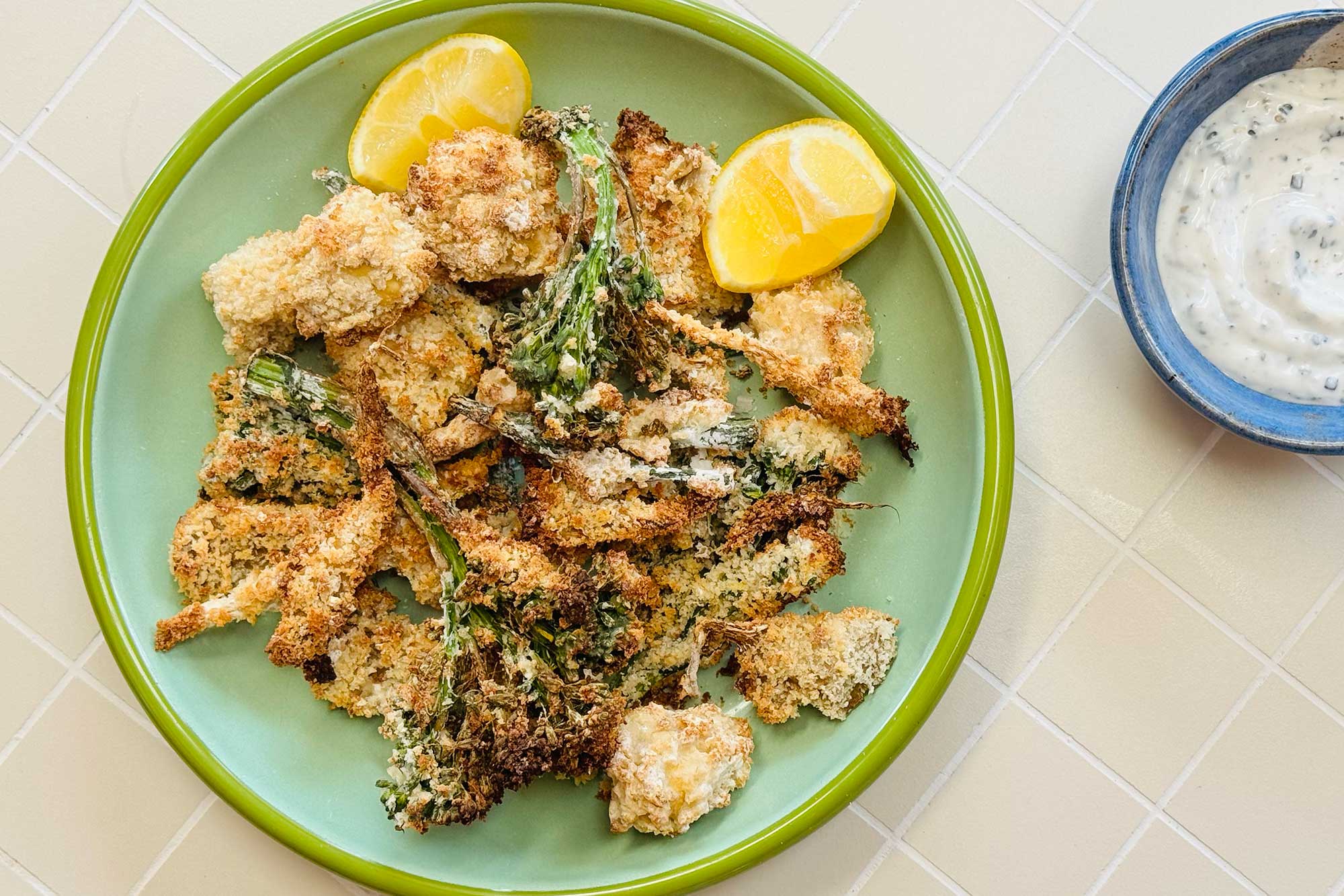 A selection of battered, air-fried vegetables on a green plate with lemon wedges.
